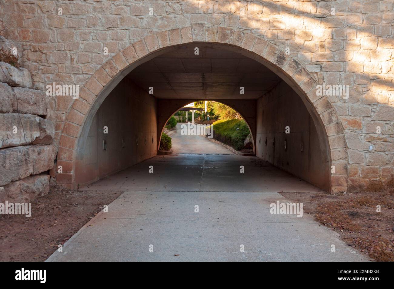 Una passerella pedonale sotto un ponte che conduce ad un lussureggiante giardino con fiori. Il lussuoso edificio dell'Aphrodite Hills Hotel and Resort con splendidi giardini Foto Stock