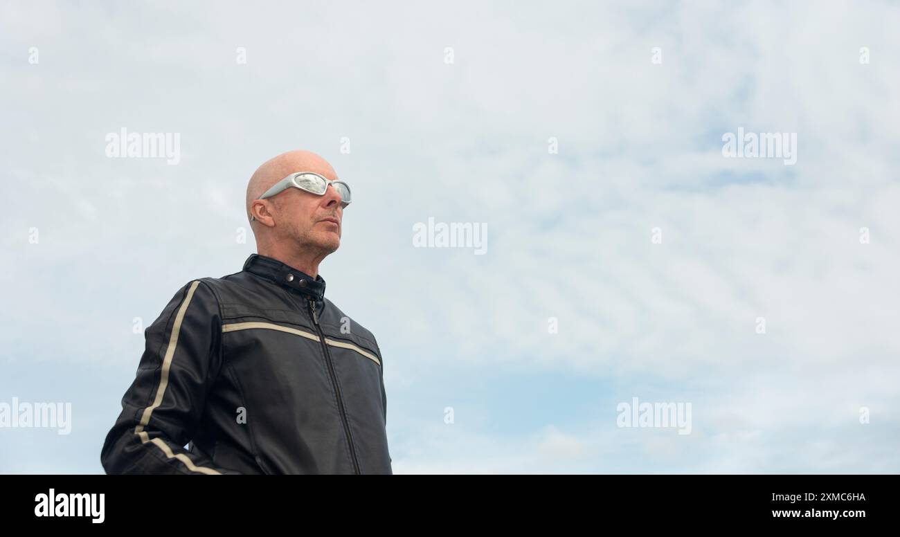 Uomo calvo con occhiali da sole e giacca in pelle. All'aperto con sfondo blu Foto Stock