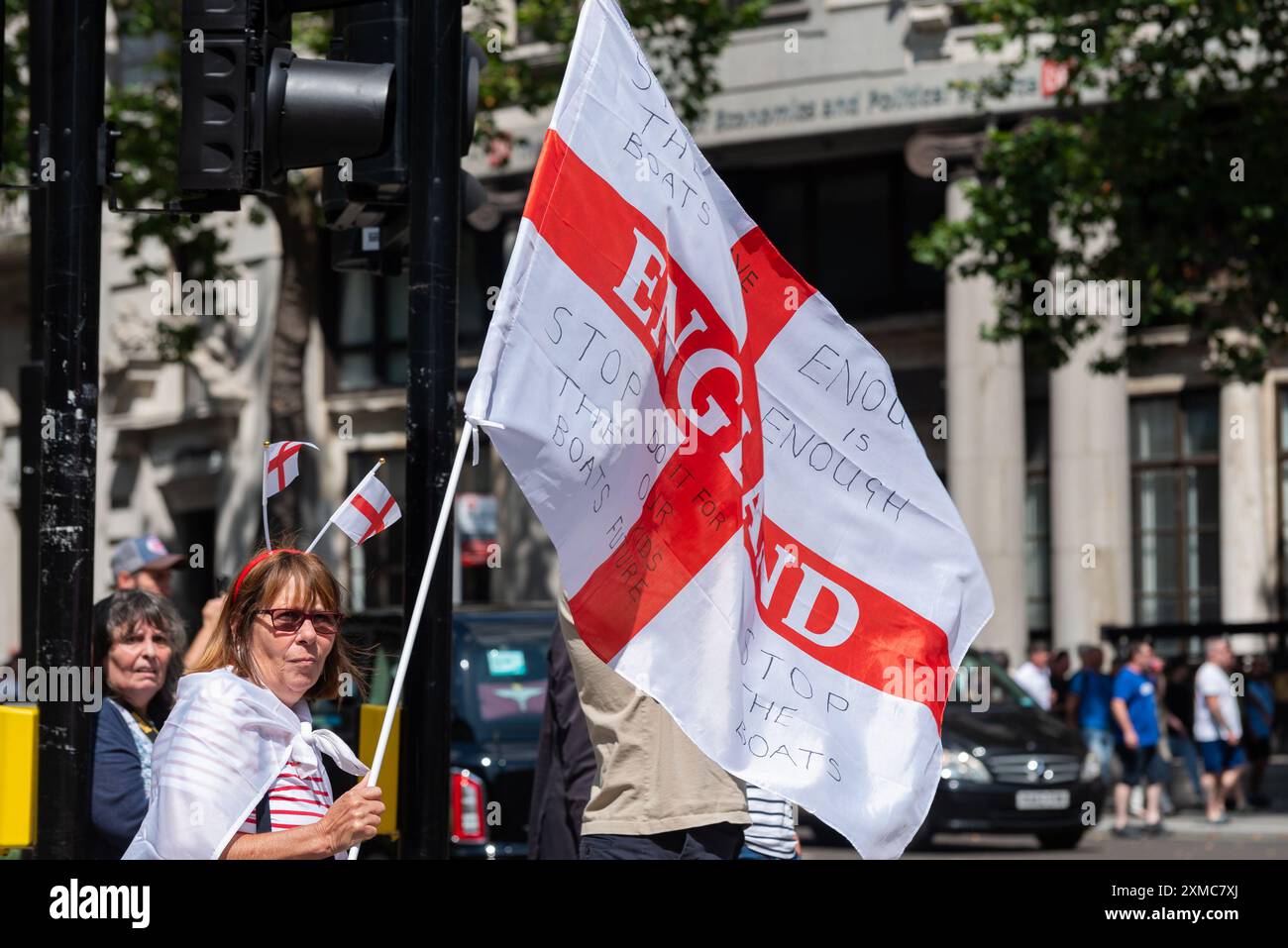 Westminster, Londra, Regno Unito. 27 luglio 2024. I sostenitori di Tommy Robinson si riunirono nello Strand presso la Royal Courts of Justice per una marcia di protesta verso Trafalgar Square. I temi della protesta includono l'immigrazione, e una protesta avversaria organizzata da Stand Up to Racism si sta dirigendo verso la vicina Whitehall con 1000 agenti di polizia in servizio per scoraggiare gli scontri. Ferma il messaggio della nave sulla bandiera inglese Foto Stock