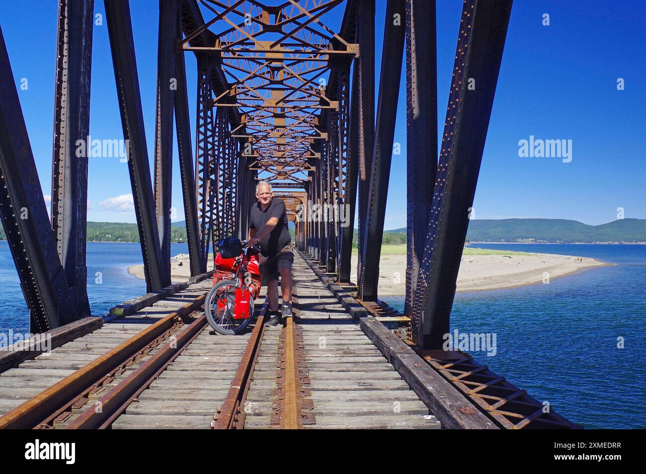 Un ponte ferroviario attraversato da una persona in bicicletta sul mare, circondato dalla natura e dai cieli blu, gite in bicicletta, vacanze avventurose, Gaspesie, St. Foto Stock