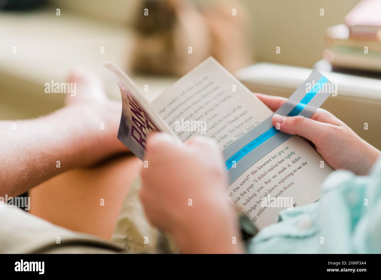 Un bambino che indossa una camicia verde chiaro e pantaloncini cachi si rilassa su un divano beige, usando una sovrapposizione verde per leggere un libro più facilmente. Questo momento cattura la dedizione del bambino al superamento della dislessia attraverso l'uso di ausili per la lettura, evidenziando l'importanza di un'istruzione accessibile. La scena è ambientata in un ambiente confortevole, che enfatizza il relax e l'apprendimento mirato. Ideale per temi legati all'infanzia, alla dislessia, agli ausili educativi, alle attività estive e all'educazione inclusiva. Foto Stock