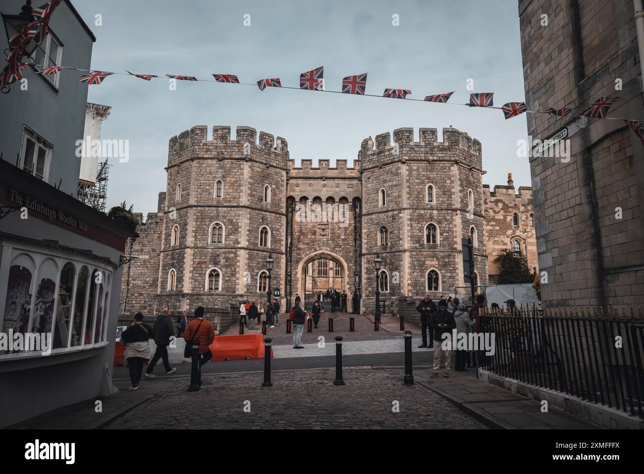 Windor Castle, UK - 16 ottobre 2023: Vista su un vecchio edificio in pietra con una grande porta ad arco. La gente passa e ci sono bandiere britanniche appese Foto Stock