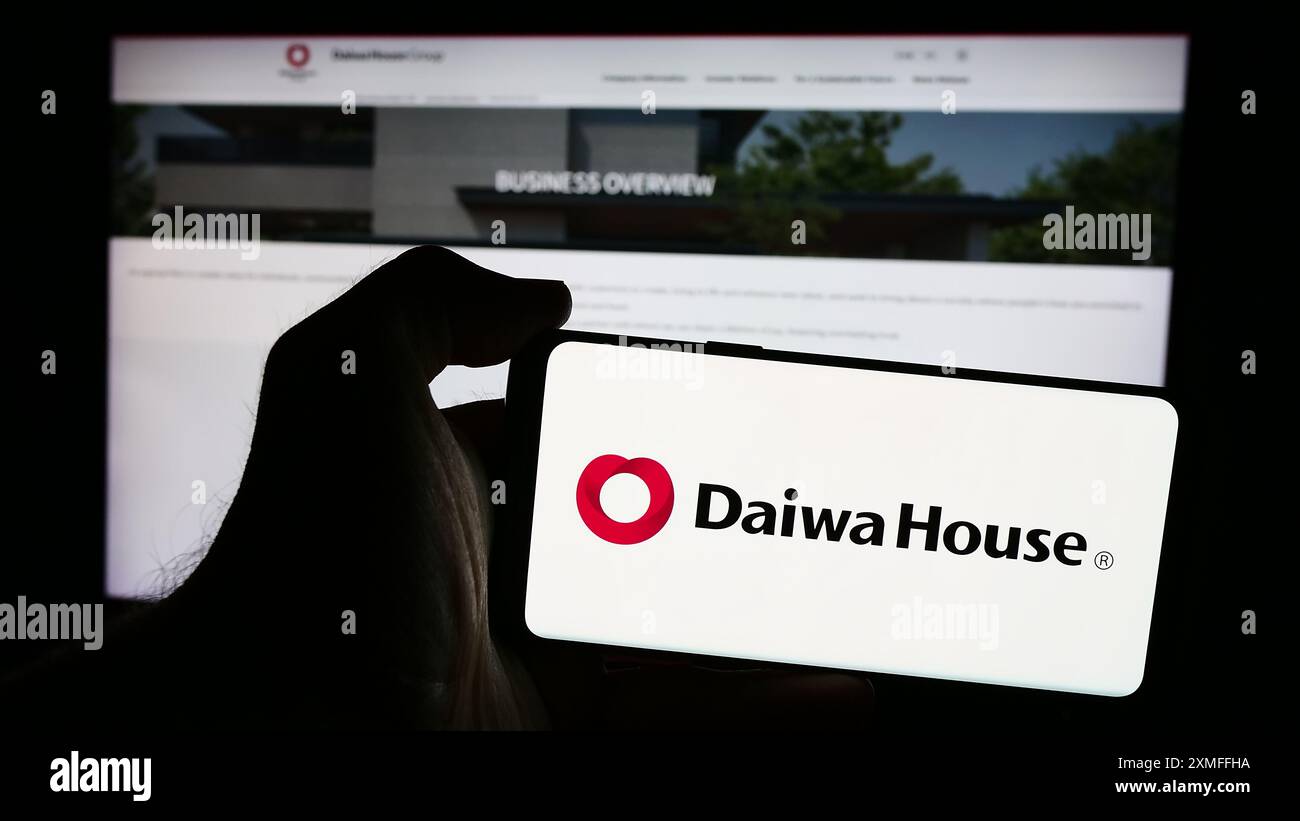 Persona che detiene lo smartphone con il logo della società di costruzioni Daiwa House Industry Co. Ltd. Davanti al sito Web. Mettere a fuoco il display del telefono. Foto Stock