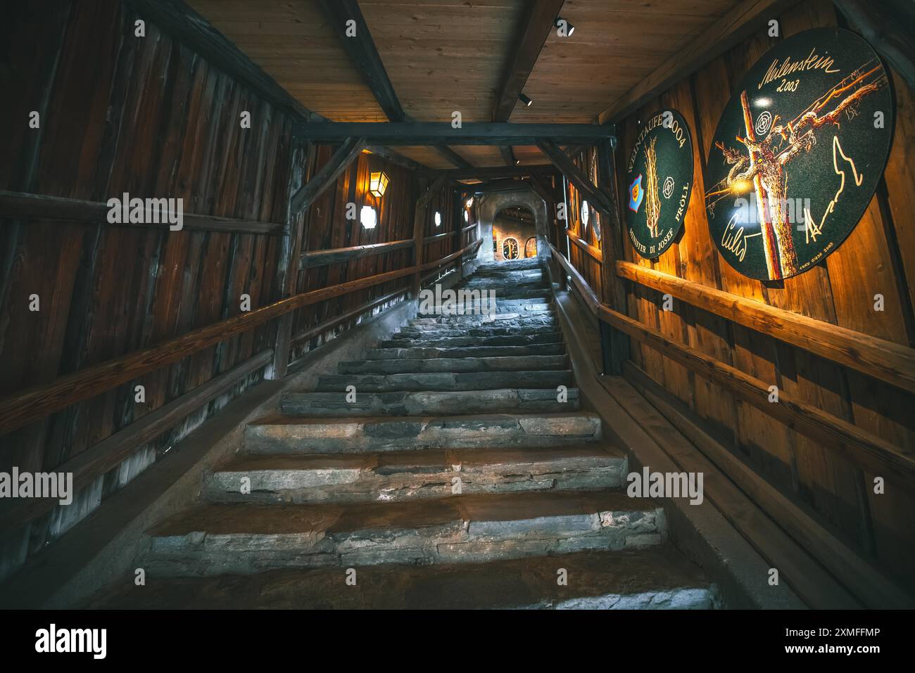 Austria - 26 ottobre 2023: Una scala in pietra si snoda verso l'alto all'interno di un edificio in legno poco illuminato. Le pareti sono fiancheggiate da tavole di legno e decorate Foto Stock