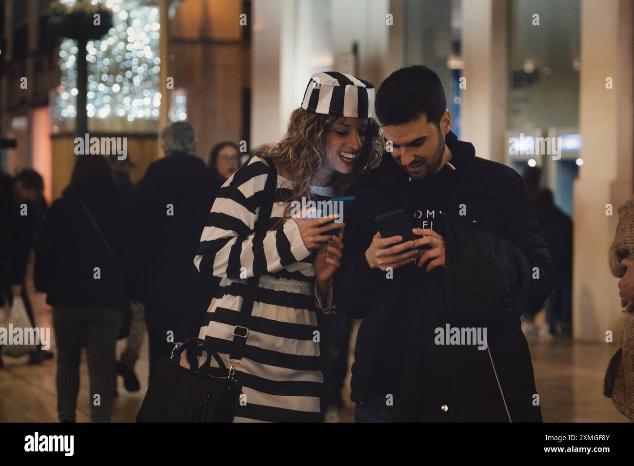 una donna e un uomo vicini che guardano uno smartphone, che l'uomo tiene in mano. La donna sorride. Indossa un abbigliamento a righe Foto Stock una donna e un uomo vicini che guardano uno smartphone, che l'uomo tiene in mano. La donna sorride. Indossa un abbigliamento a righe Foto Stock