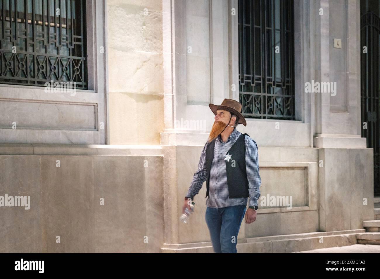 Uomo mascherato con barba in un abito con stemma stellare, accanto a un classico edificio in pietra, elegantemente rivestito con giacca in denim e jeans blu. Foto Stock Uomo mascherato con barba in un abito con stemma stellare, accanto a un classico edificio in pietra, elegantemente rivestito con giacca in denim e jeans blu. Foto Stock