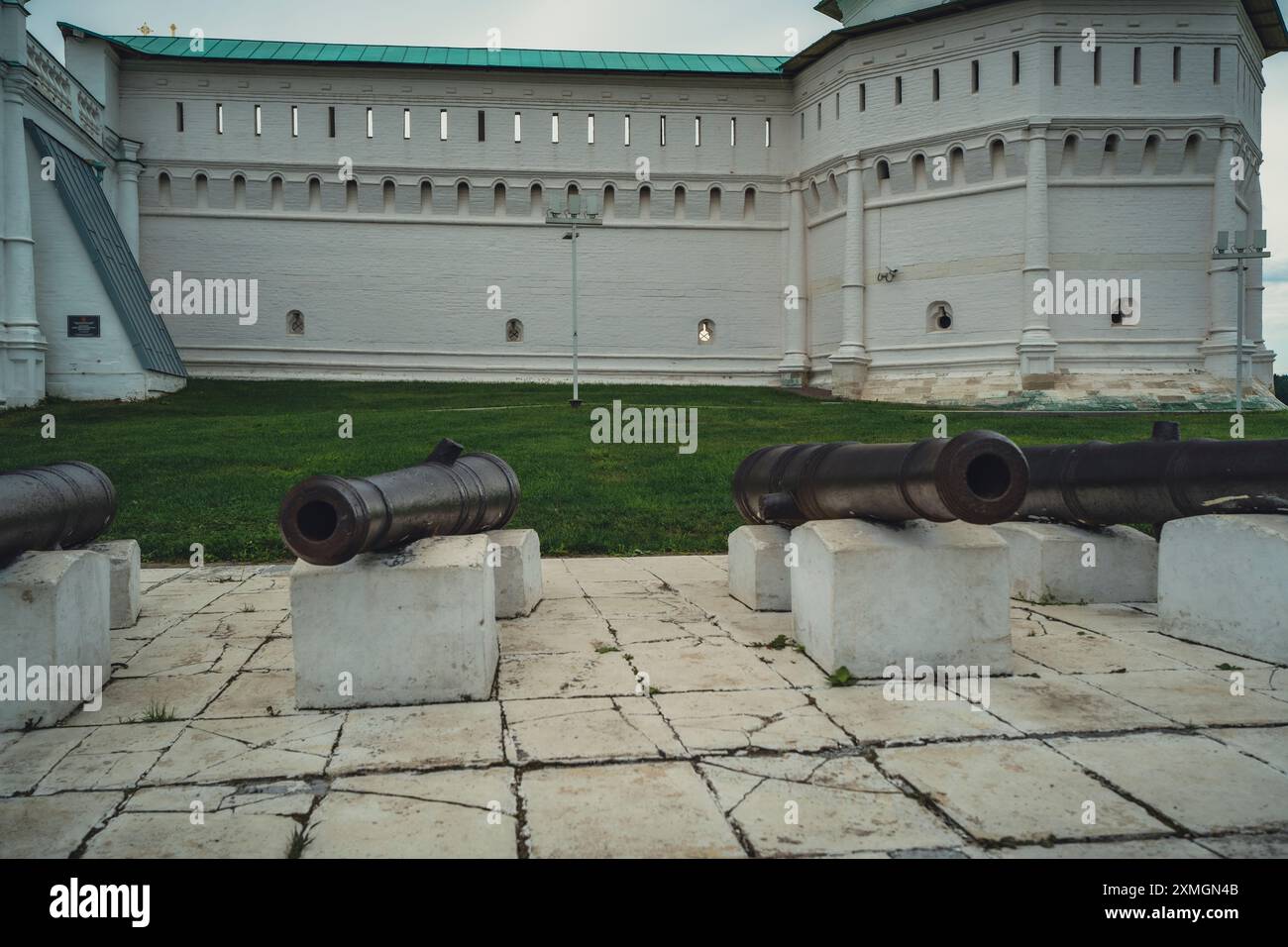 Cannoni arrugginiti su piattaforme di pietra di fronte a una storica fortezza muraria, che mette in risalto il patrimonio militare sotto un cielo nuvoloso. Foto Stock