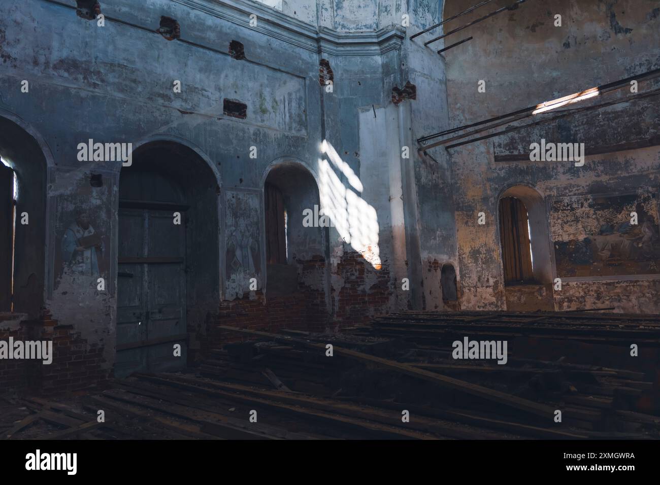 Interno di una chiesa abbandonata con porte ad arco e muri in decadenza, illuminati dalla luce del sole attraverso una finestra. Foto Stock