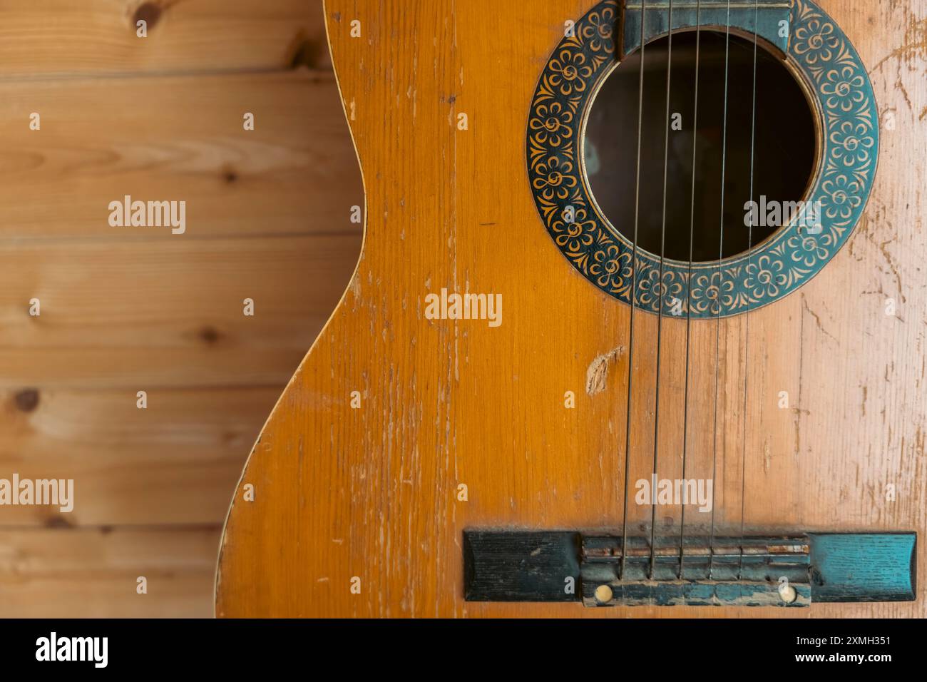 Una vecchia chitarra acustica ben indossata con graffi e segni visibili, appesa su una parete di legno. La chitarra ha una rosetta dettagliata intorno al buco del suono, Foto Stock