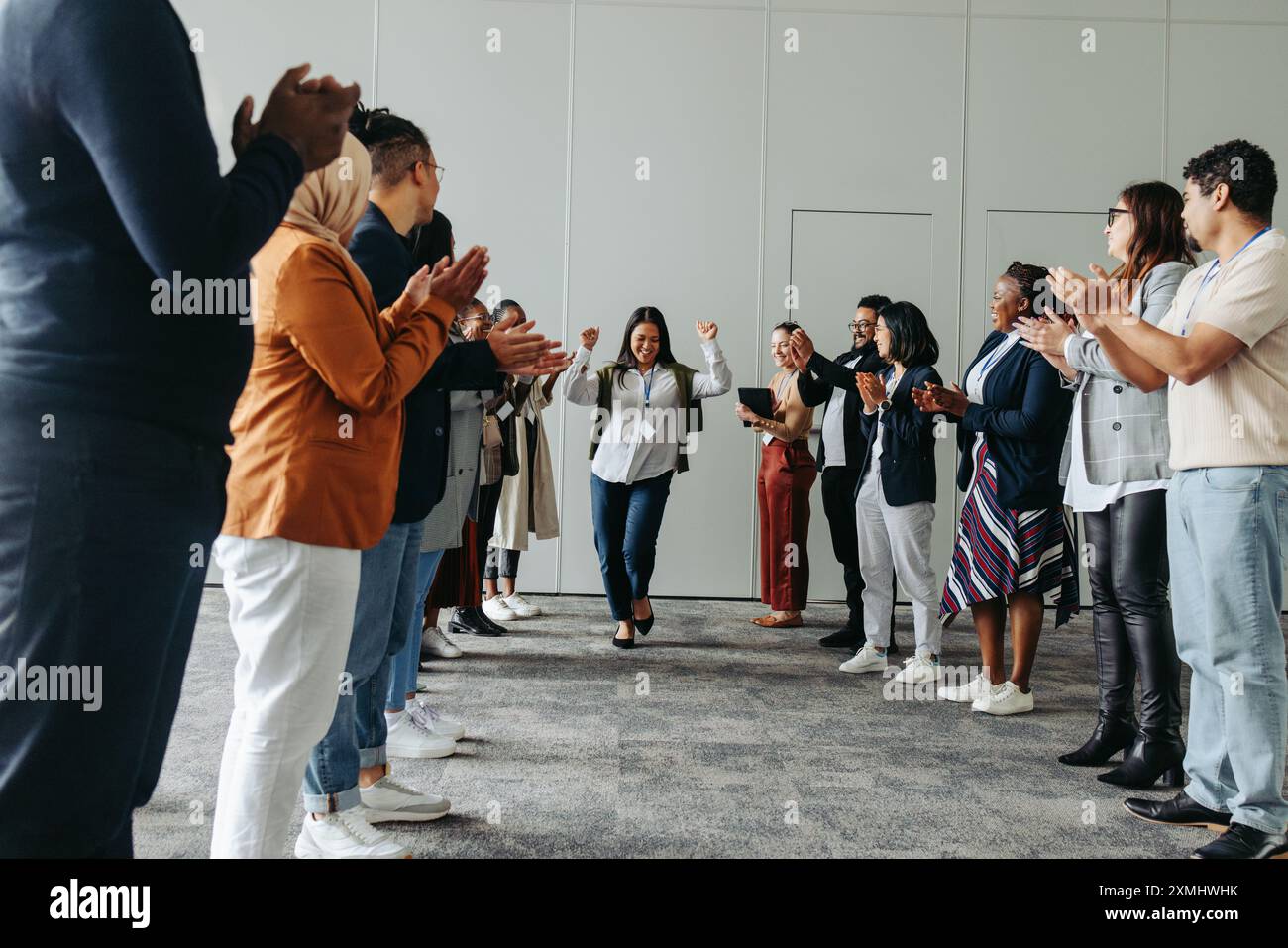 Un gruppo eterogeneo di professionisti che applaudiscono e celebrano una donna in un ambiente aziendale, riflettendo il lavoro di squadra, i successi e l'inclusività Foto Stock
