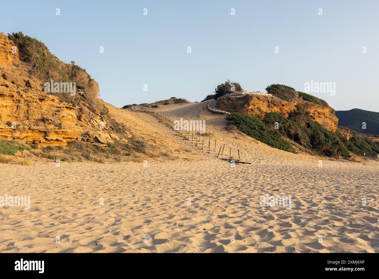 Spiaggia sabbiosa illuminata dal sole con sentiero in legno. Di Scivu Foto Stock