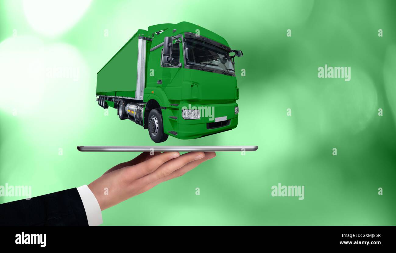 Mano con tablet digitale e camion verde. Concetto di gestione delle flotte ecologiche. Foto Stock