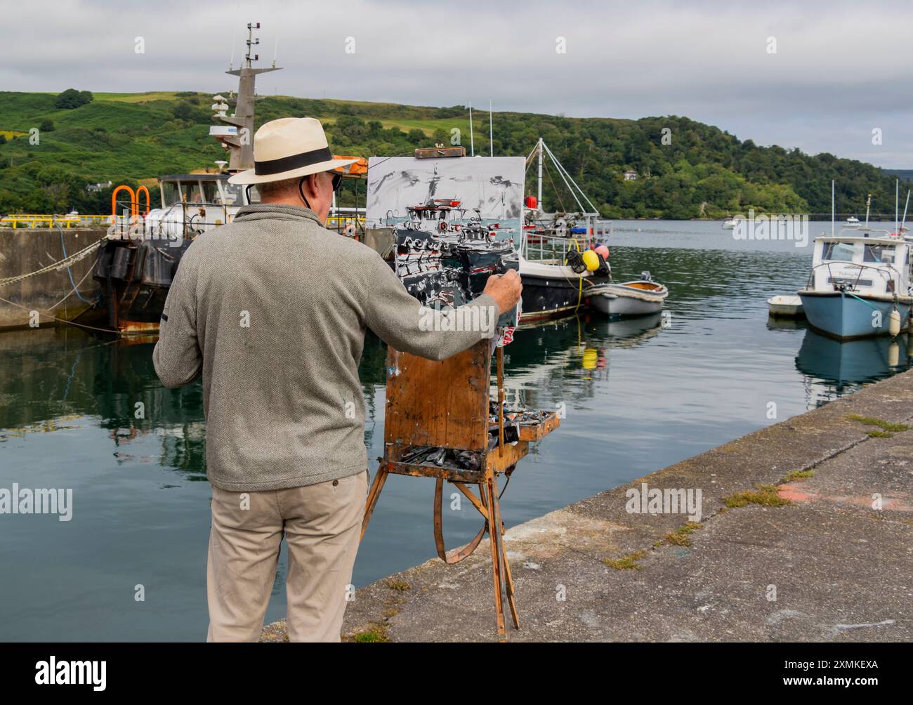 Artista maschile che dipinge scene all'aperto da un molo. Union Hall, West Cork, Irlanda Foto Stock