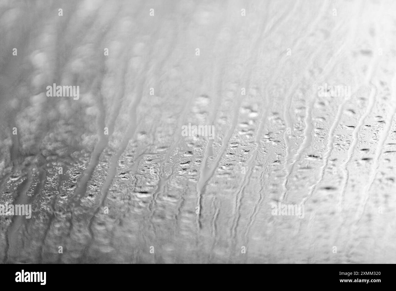 Gocce di pioggia e gocce verticali su una finestra di vetro durante un temporale nel pomeriggio. Trama di sfondo. Foto Stock