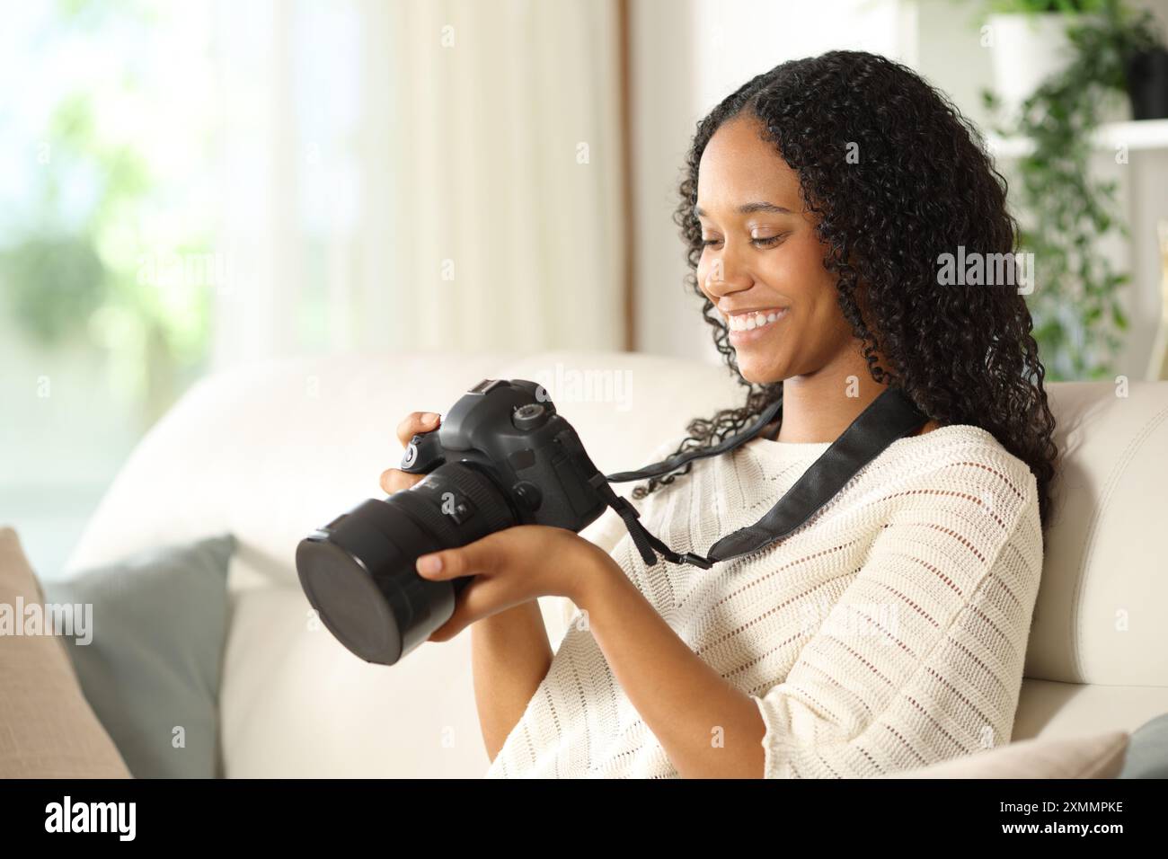 Felice fotografo nero che controlla la fotocamera seduto su un divano di casa Foto Stock