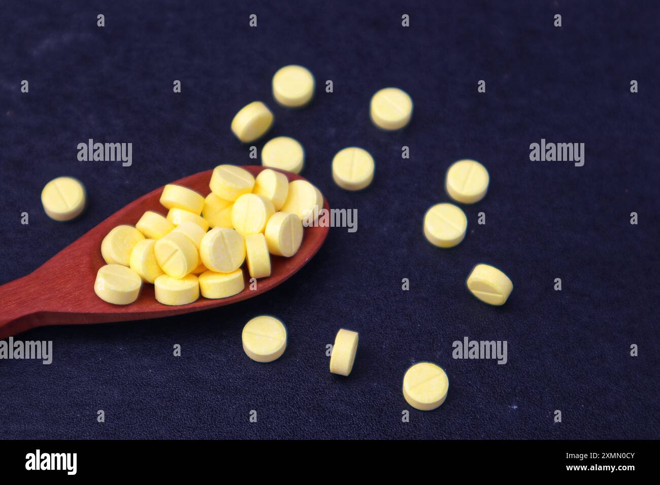 Compresse di medicina gialla o vitamina C in un cucchiaio di legno e alcune sparse in vista ravvicinata su sfondo nero. Foto Stock