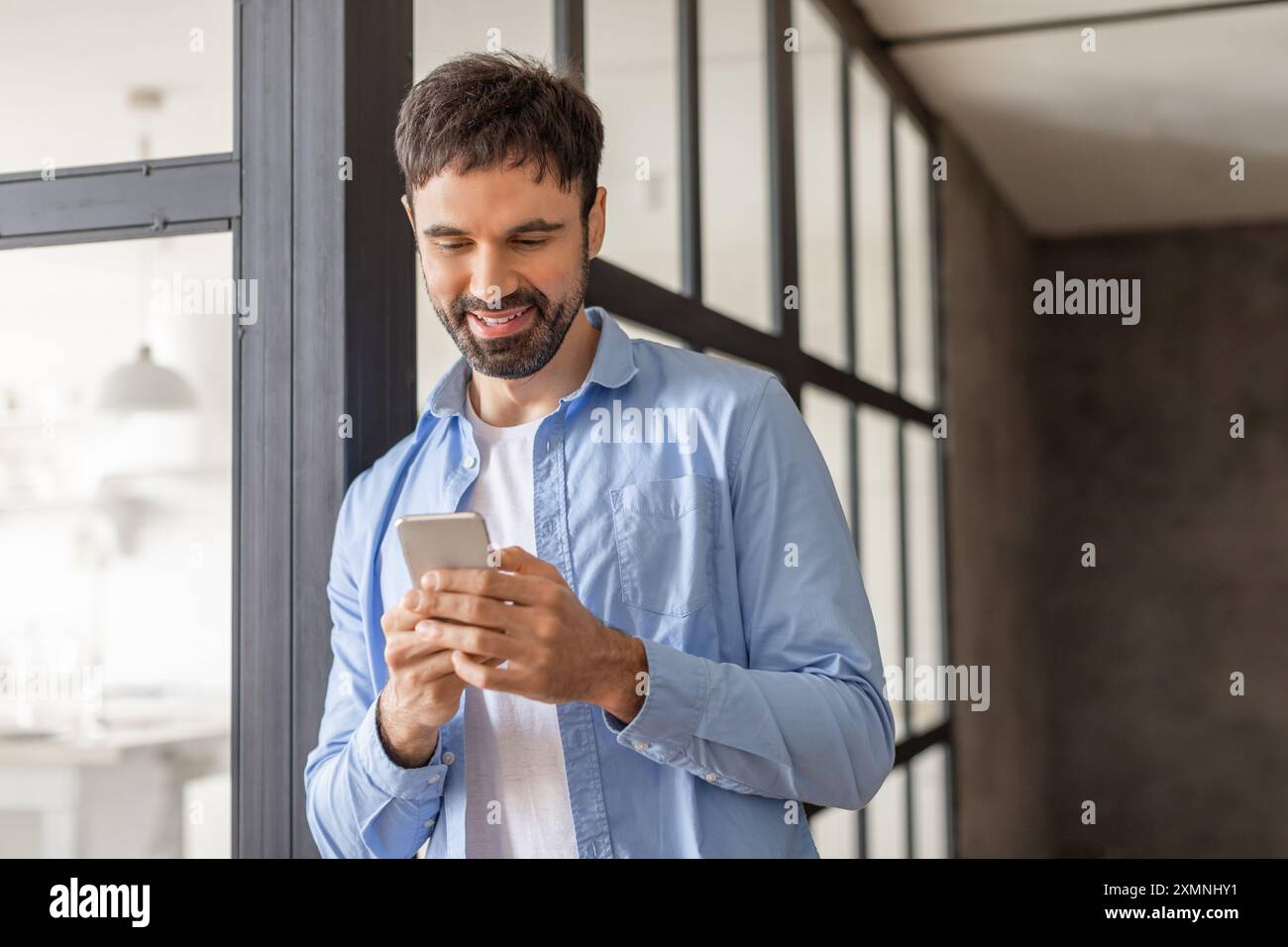 Uomo sorridente mentre utilizza lo smartphone in un ambiente ufficio moderno Foto Stock