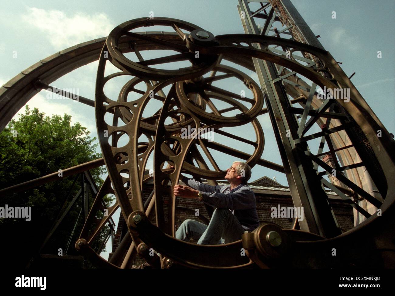 Il Dr Jonathan Minns fondatore e direttore del British Engineerium Hove con la sua scultura cinetica "Water Cycle", il Dr Jonathan Minns fondatore e direttore del British Engineerium Hove si trova all'interno del movimento eccentrico di un'enorme ruota ad acqua scultorea meccanica composta da 1713 parti separate. La ruota e base in bronzo da tredici tonnellate e mezzo chiamata Water Cycle è stata commissionata da Hong Kong Land PTE per Raffles Square a Singapore . La scultura cinetica progettata dal dottor Minns ha impiegato due anni per costruirla. Foto di Roger Bamber 17 settembre 2000 Foto Stock