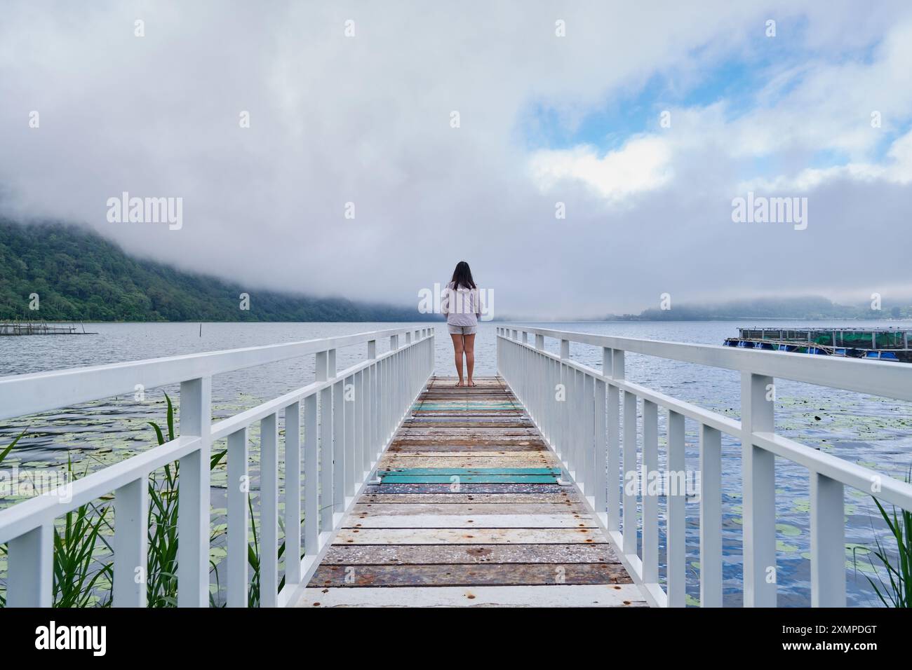 Una ragazza in piedi sul bordo del ponte sul lago Bedugul, Bali Foto Stock