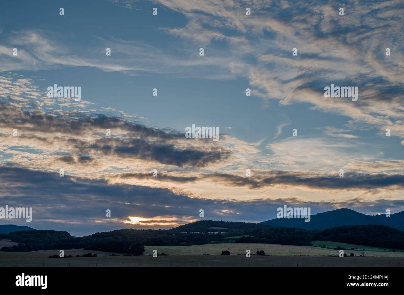 Paesaggio rurale estivo al tramonto. Con un cielo nuvoloso e colorato. Il sole dietro le nuvole. Colline sullo sfondo. Chocholna, Slovacchia Foto Stock