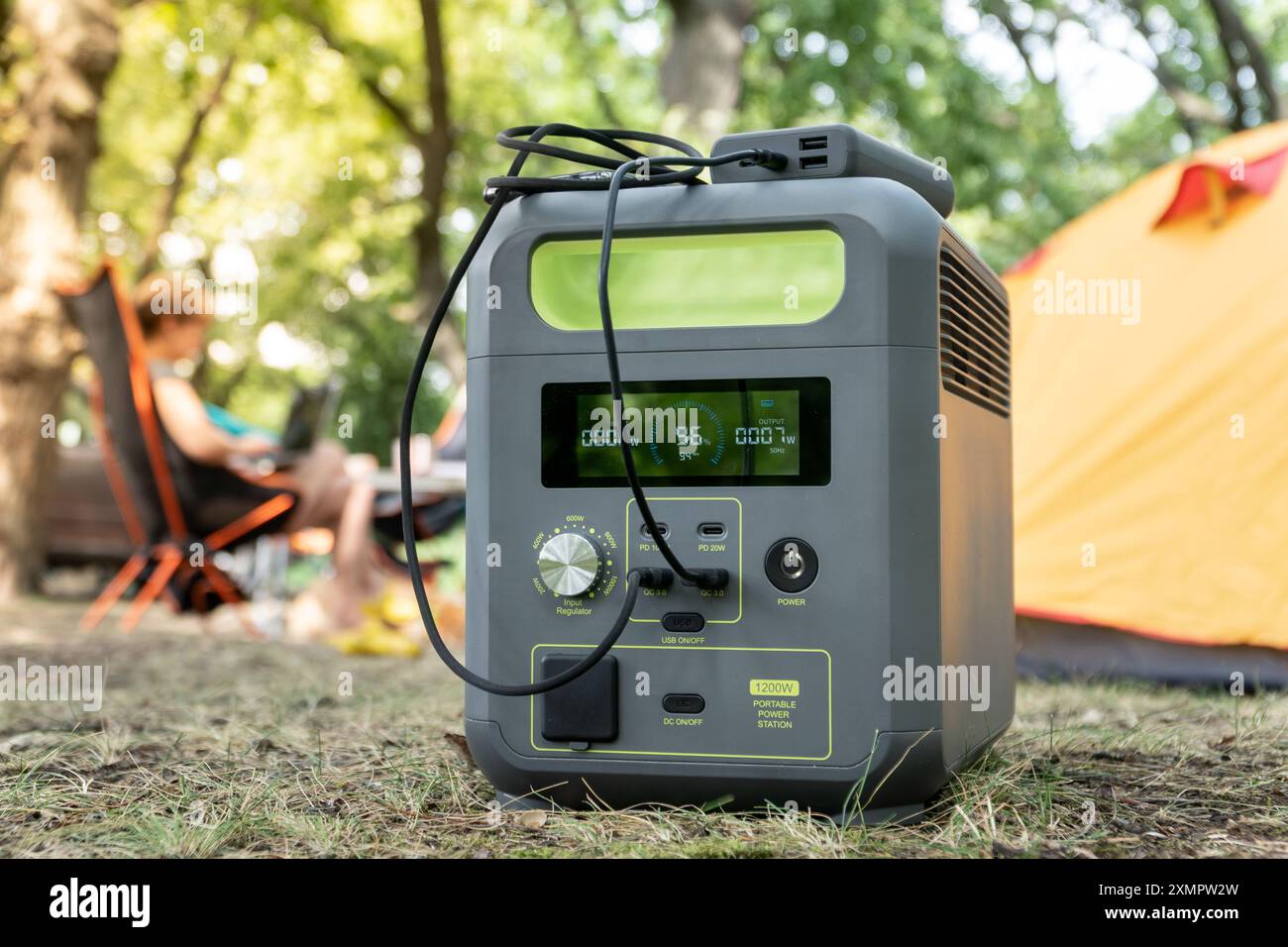 Centrale elettrica portatile con batteria al litio-ferrofosfato che carica i dispositivi elettronici utilizzati in un campo selvaggio, di fronte alla tenda gialla. Portatile Foto Stock