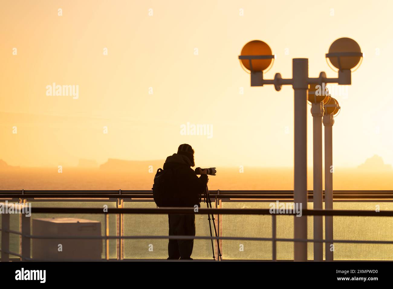 Nave da crociera al tramonto Antartide passeggero maschio fotografo professionista con teleobiettivo a cappello caldo treppiede luce solare calda ora magica Foto Stock