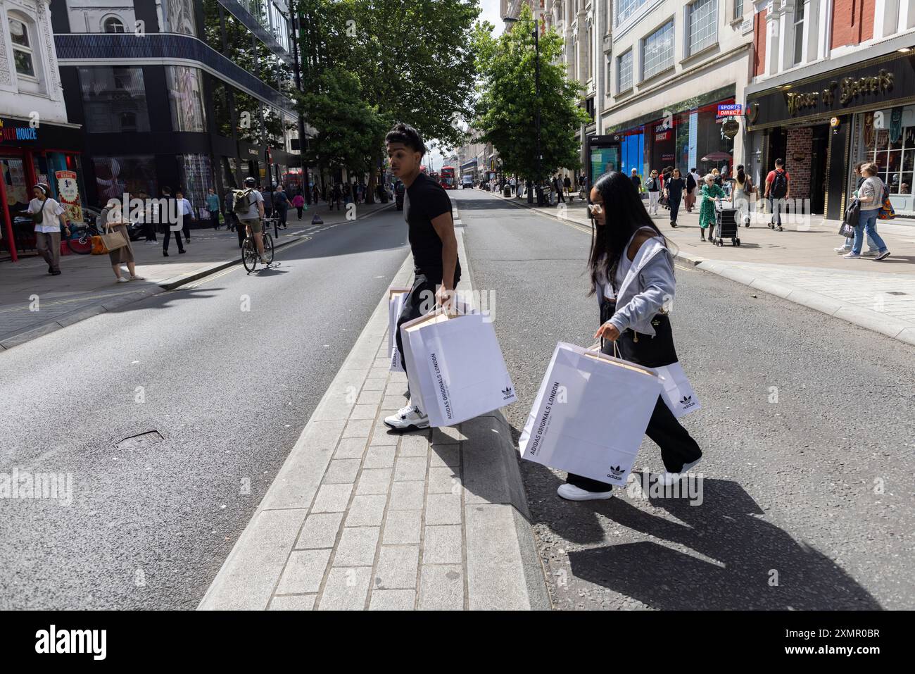 Giovane coppia che trasporta borse della spesa Adidas attraverso New Oxford Street nel West End di Londra, Inghilterra, Regno Unito Foto Stock