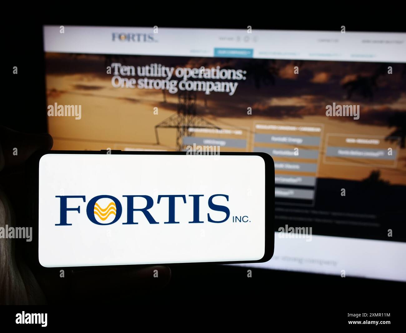 Persona che possiede uno smartphone con il logo dell'azienda canadese Fortis Inc. Davanti al sito Web. Mettere a fuoco il display del telefono. Foto Stock