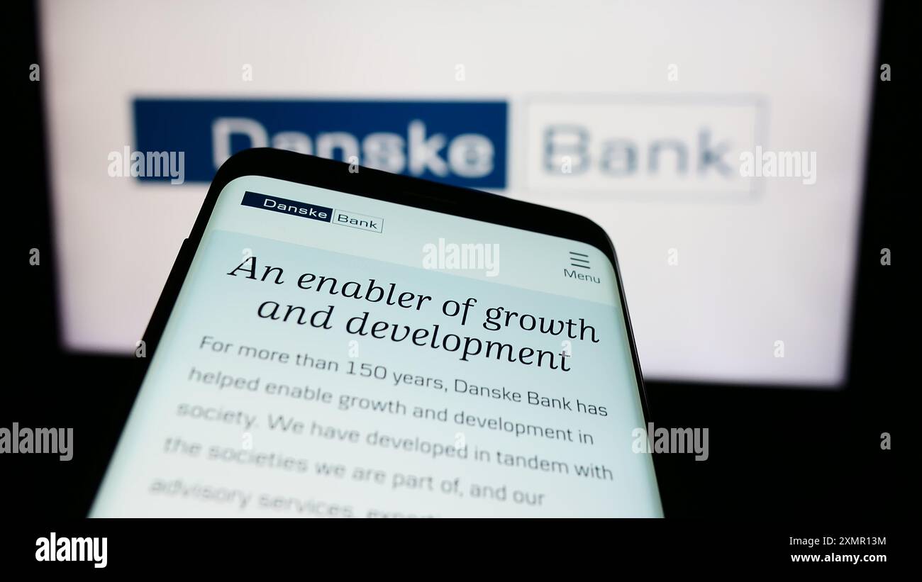 Smartphone con sito web della società danese di servizi finanziari Danske Bank davanti al logo aziendale. Mettere a fuoco in alto a sinistra sul display del telefono. Foto Stock