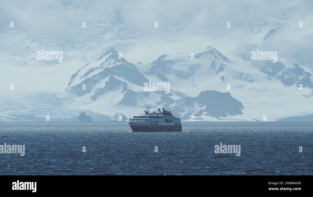 Nave da spedizione con vista laterale in Antartide con enormi montagne coperte di neve destinazione remota crociera panoramica ampia vista esplorando l'Artico Foto Stock