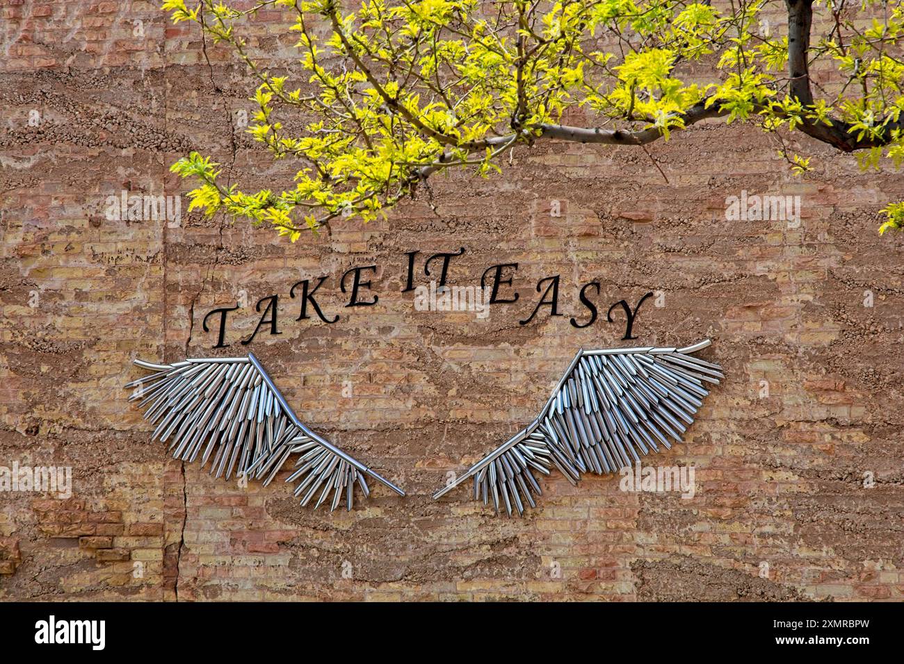 Le ali artistiche di metallo abbelliscono il muro di mattoni commemorando la hit song degli Eagles 'Take IT Easy' nel centro di Winslow, Arizona, aprile 2024 Foto Stock