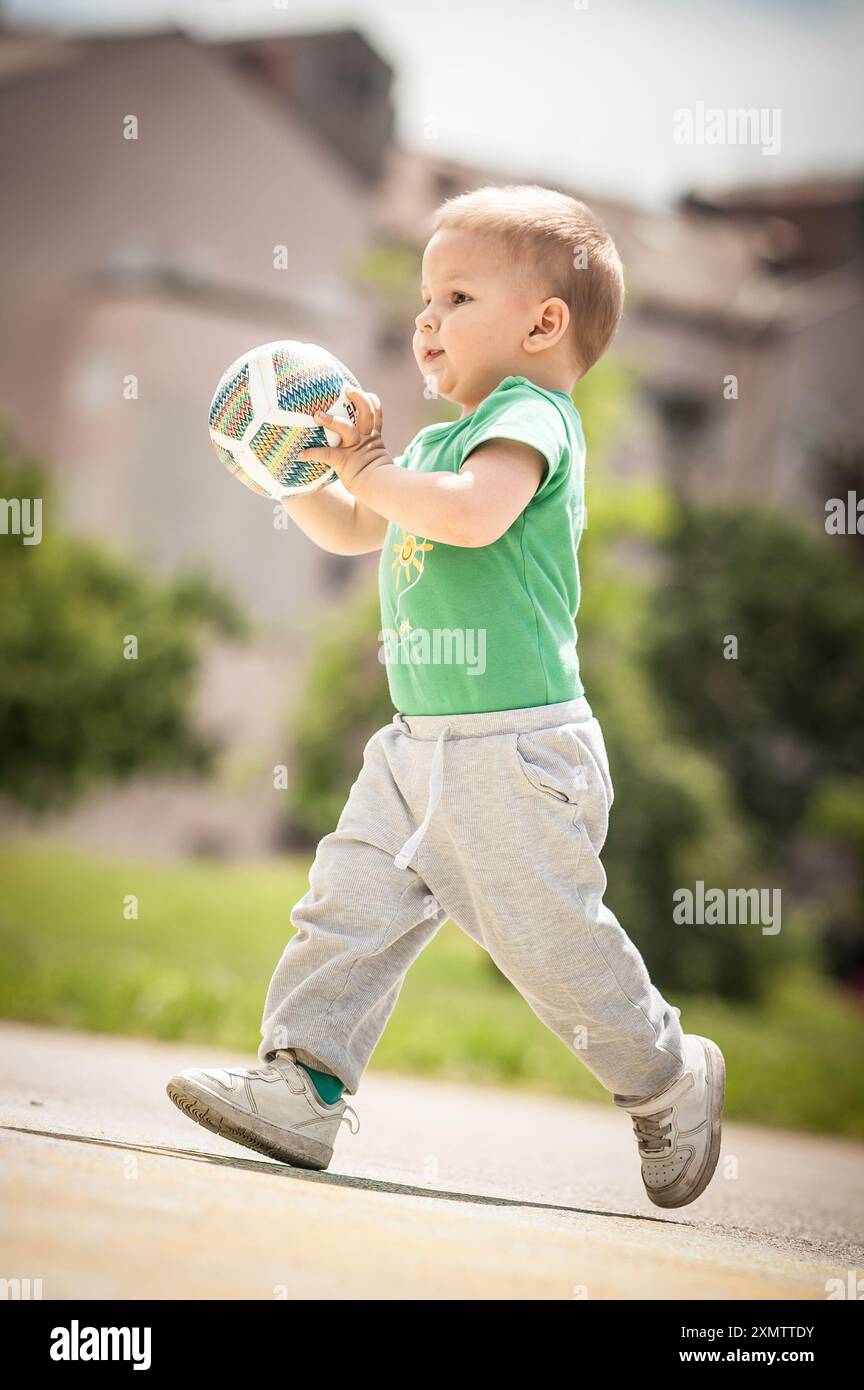 Piccolo simpatico che si diverte a giocare con la palla colorata nel parco. Splendida giornata di sole autunnale nel parco giochi per bambini Foto Stock