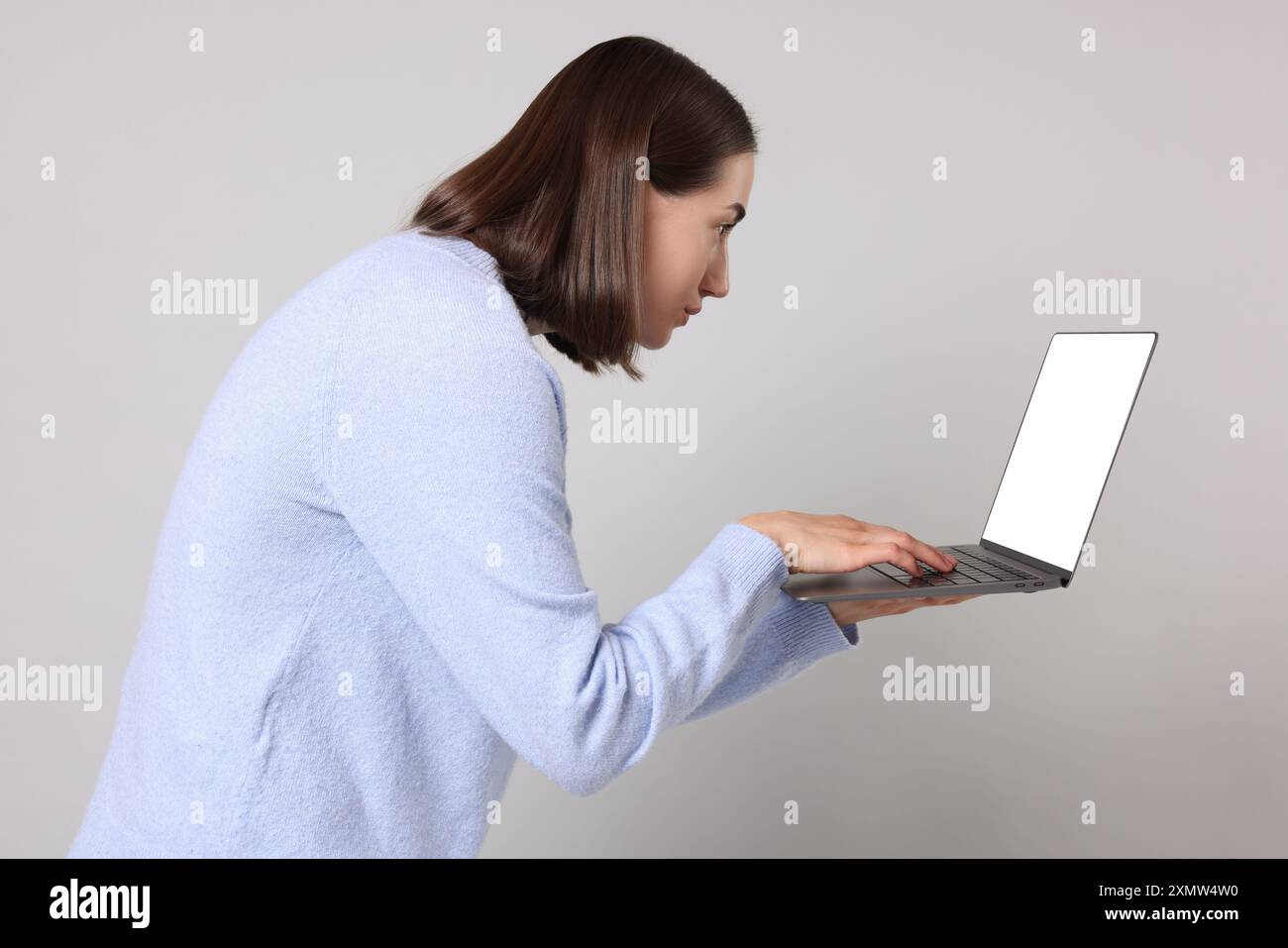 Donna con postura scarsa che utilizza un notebook su sfondo grigio Foto Stock