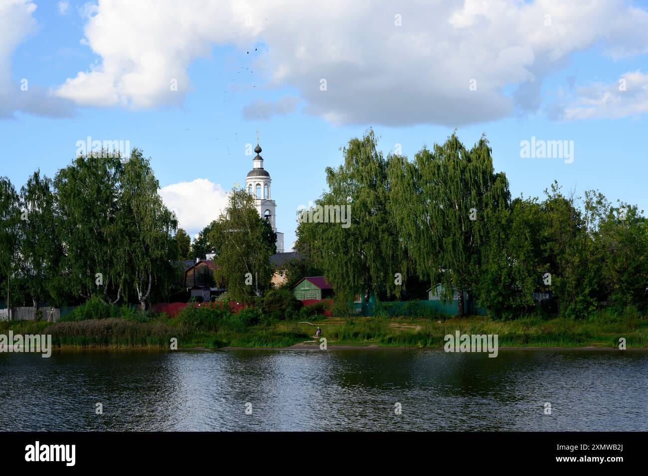 Alberi fitti e case in legno sulle rive del fiume Volga con sopra il campanile del monastero di Tolga, vicino a Yaroslavl, Russia Foto Stock