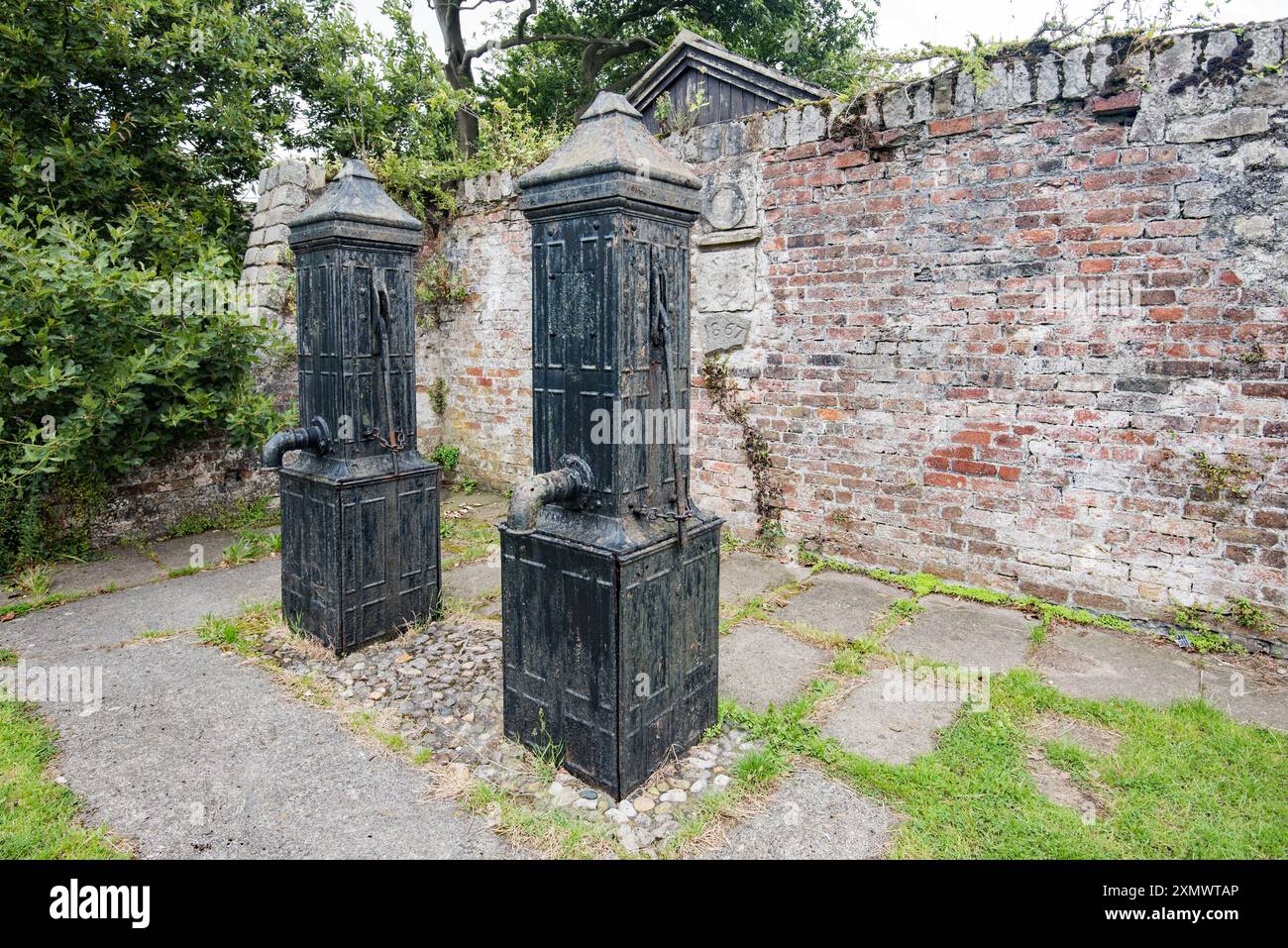 Pompe dell'acqua sul lato S e nel parco del David Hughes Community Centre, con fossato del castello sul lato e e una sezione restituita di un muro rivestito in mattoni Foto Stock