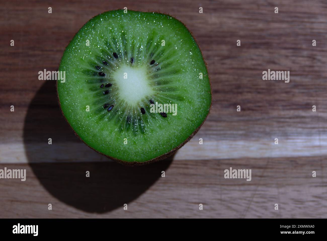 Un kiwi diviso a metà siede su un tavolo di legno, che mostra la sua vibrante polpa verde e i semi neri. Foto Stock