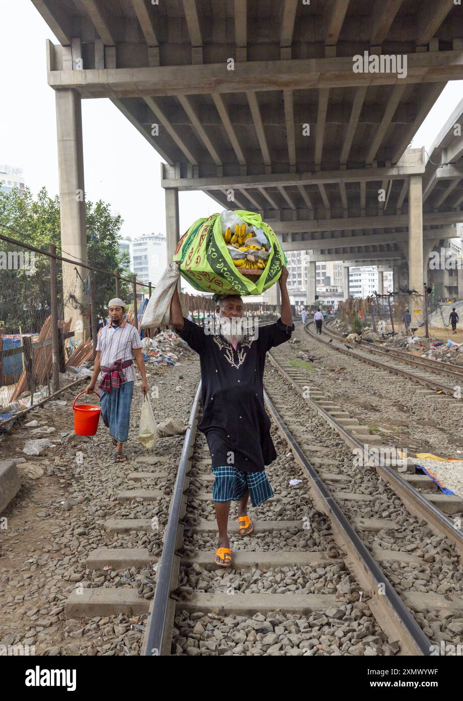 Un vecchio bengalese cammina lungo la ferrovia con una borsa sulla testa, la Divisione di Dacca, Dacca, Bangladesh Foto Stock