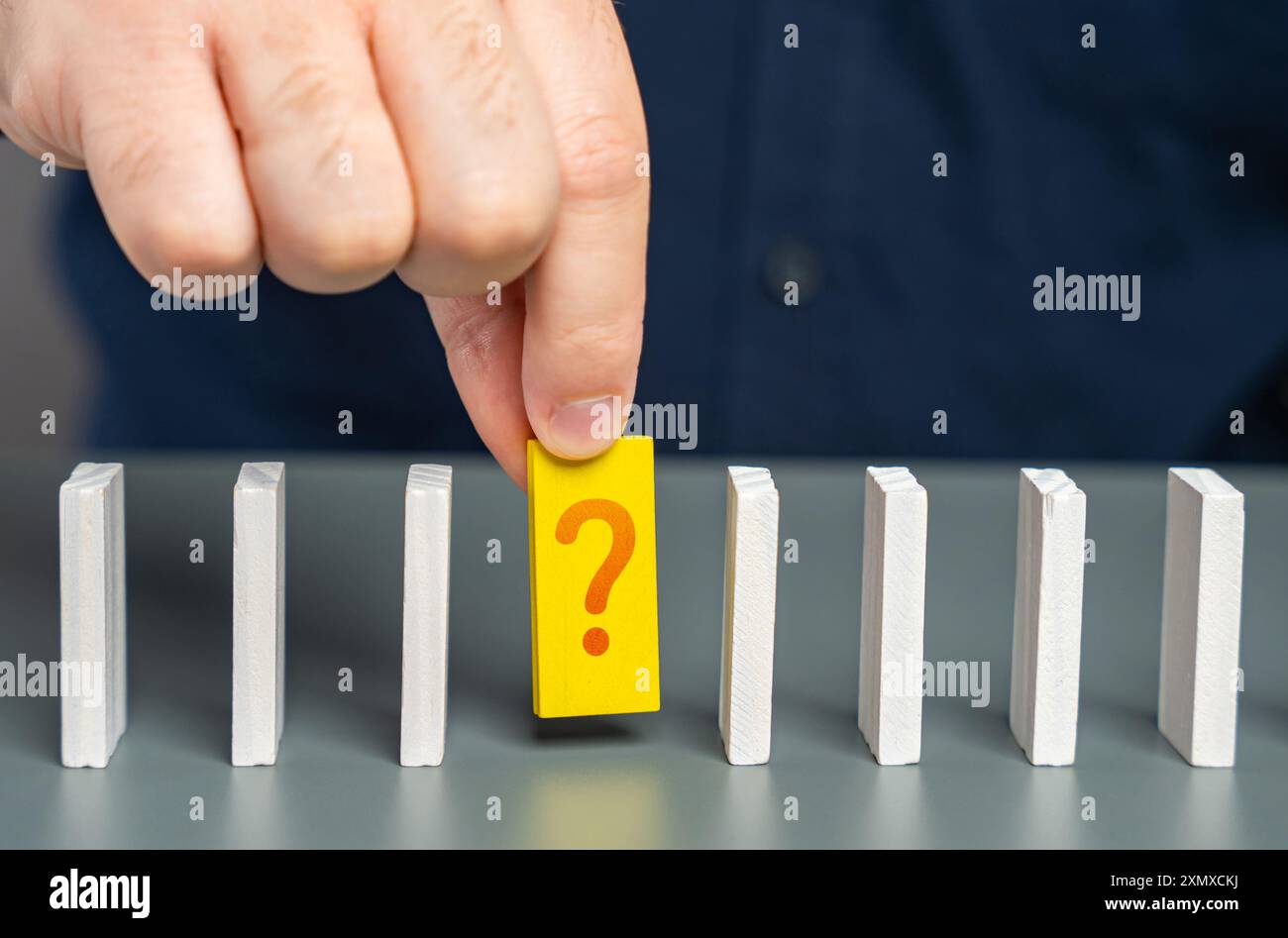 Un uomo studia un elemento sconosciuto di una catena di processi sotto forma di domino. Trovare una risposta a una domanda. Correzione degli errori. Il fatto rimane Foto Stock