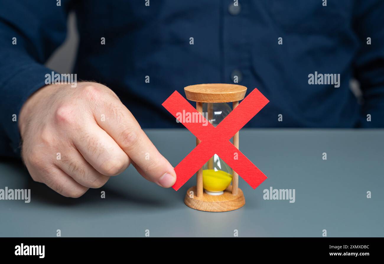 Un uomo ha una croce rossa sopra una clessidra. Fine del tempo. Blocco e divieto di ulteriori interventi. Rifiuto del tempo supplementare, cessazione del Foto Stock