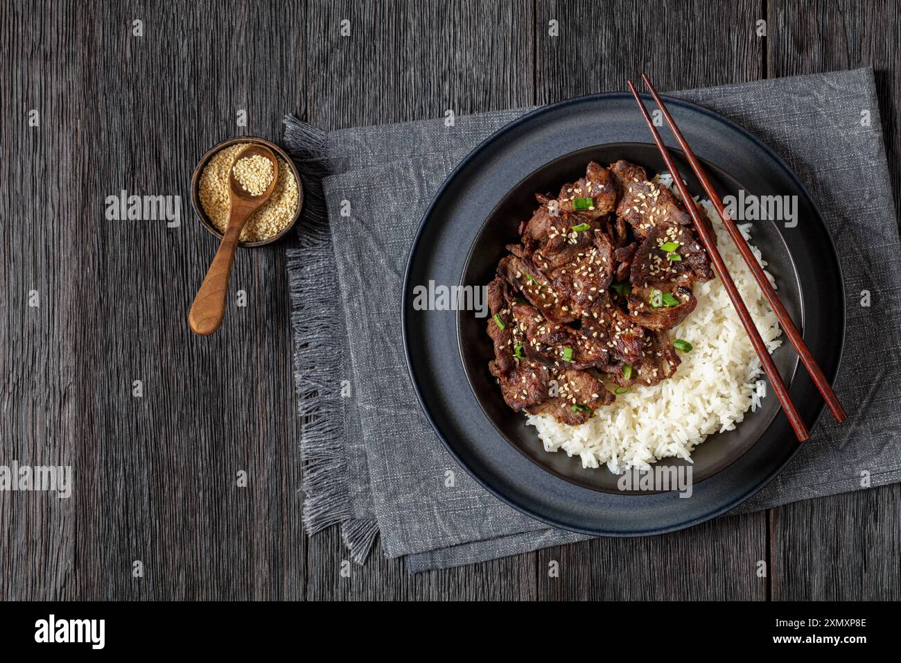 Bulgogi, manzo BBQ coreano, manzo fritto a fette sottili cosparso di semi di sesamo e cipolla primaverile servito con riso a grani lunghi nel recipiente con le bacchette Foto Stock