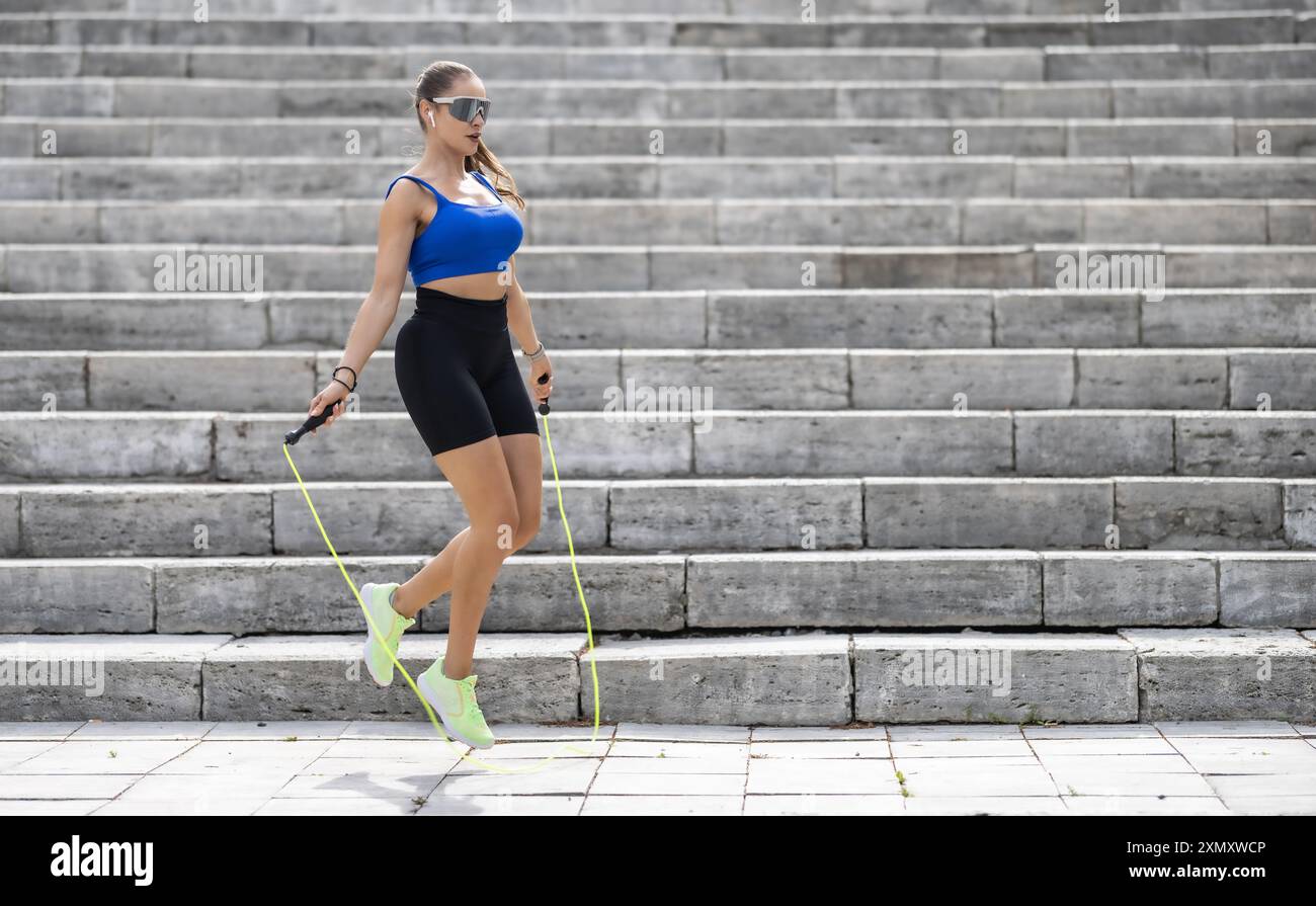 Foto all'aperto di donna in abbigliamento sportivo che si allenano con la corda per saltare all'aperto in un parco. Fitness femminile che si allena con la corda per saltare in un parco. Foto Stock