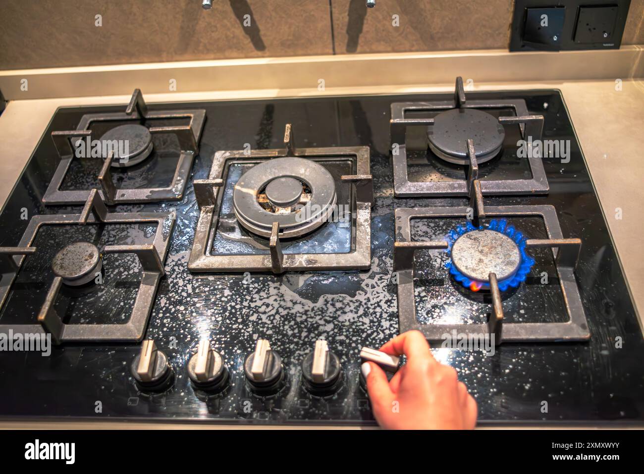 Un cuoco che tenta di accendere il fornello, mostrando l'azione di cottura della stufa durante il processo di cottura in un ambiente di cucina affollato. Foto Stock