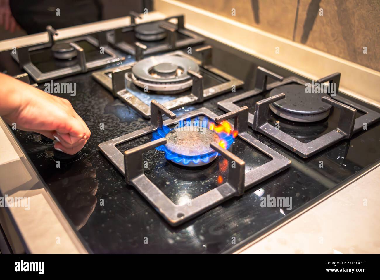 Un cuoco che tenta di accendere il fornello, mostrando l'azione di cottura della stufa durante il processo di cottura in un ambiente di cucina affollato. Foto Stock