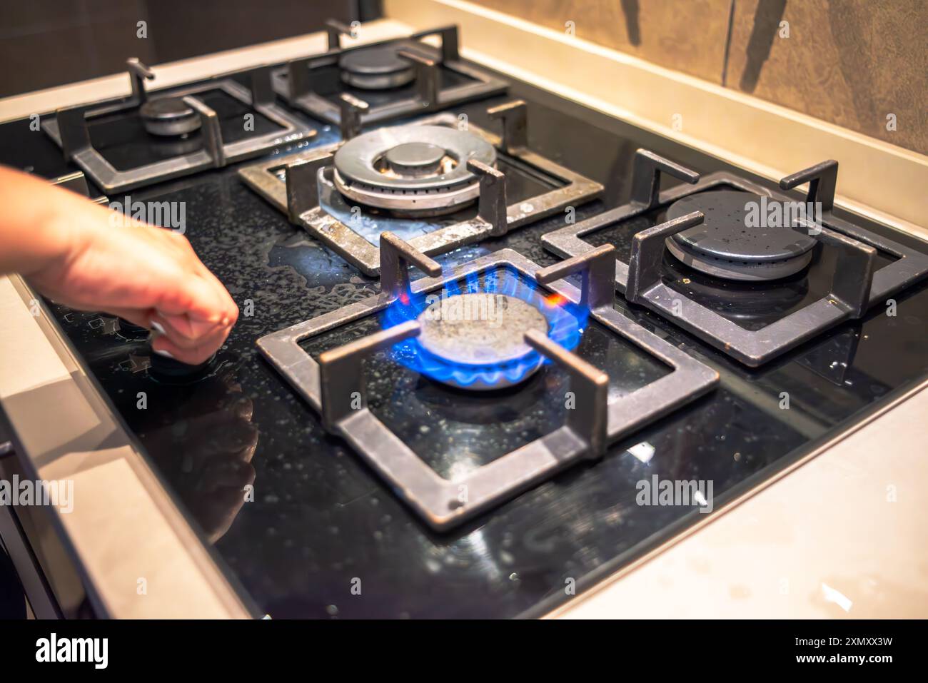 Un cuoco che tenta di accendere il fornello, mostrando l'azione di cottura della stufa durante il processo di cottura in un ambiente di cucina affollato. Foto Stock
