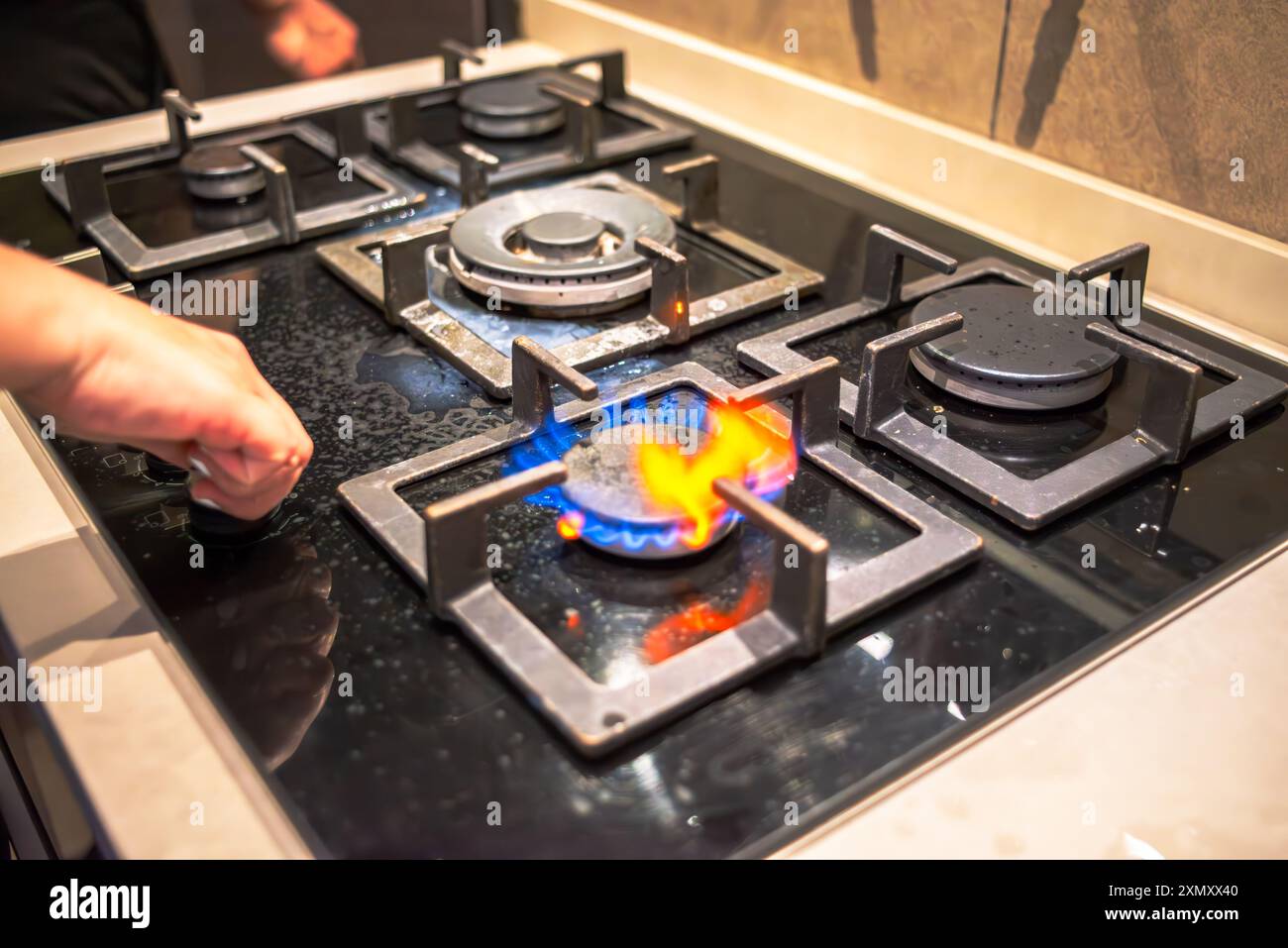 Un cuoco che tenta di accendere il fornello, mostrando l'azione di cottura della stufa durante il processo di cottura in un ambiente di cucina affollato. Foto Stock