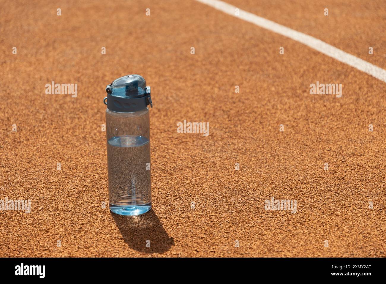 Bottiglia d'acqua blu rinfrescante nelle giornate di sole con un'ombra dura sul campo sportivo. Concetto di acqua potabile. Bilanciamento dell'acqua per la stagione calda per l'allenamento, ACT Foto Stock