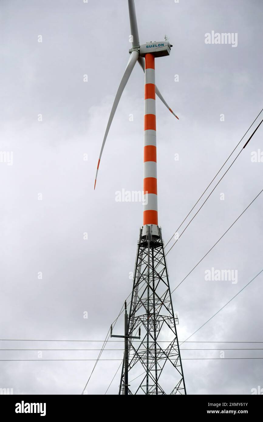 Torreggiando contro il cielo nuvoloso, una turbina eolica si erge alta e le sue tre pale sono pronte a catturare l'energia del vento. Contrassegnato con strisce arancioni e bianche Foto Stock