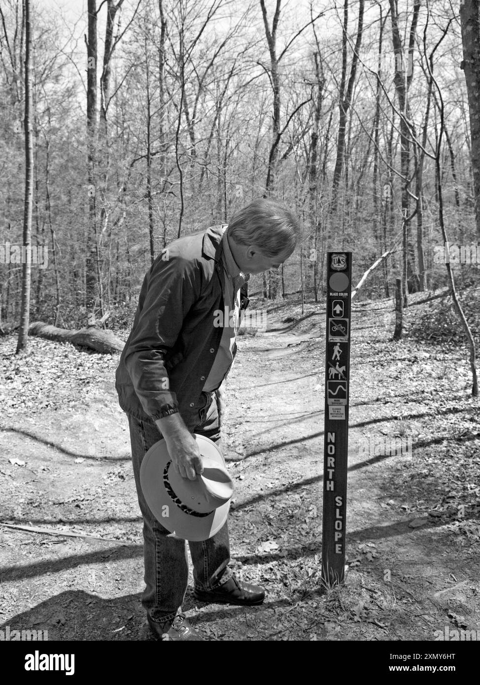 Un uomo caucasico di mezza età con una giacca blu che fa trekking su un sentiero al Davidson River Campground vicino a Brevard, NC, leggendo intensamente un cartello. Foto Stock