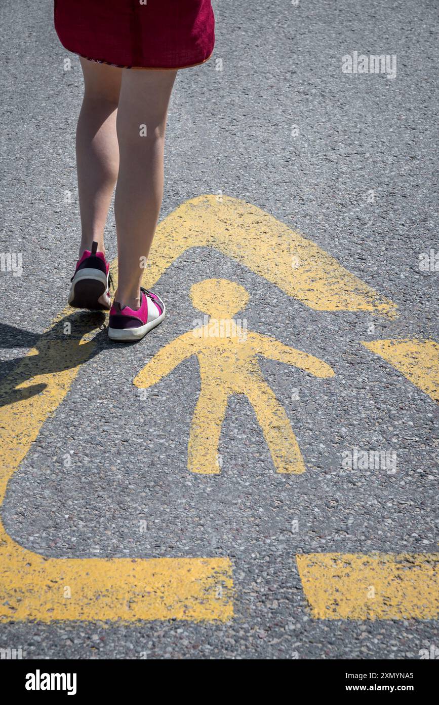 Girl Walking through Caution Children Street Sign on Asphalt Road. Attenzione bambini! Foto Stock