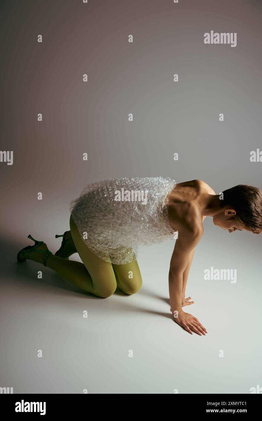 Una donna con un abito a bolle si inginocchia su un pavimento bianco. Foto Stock